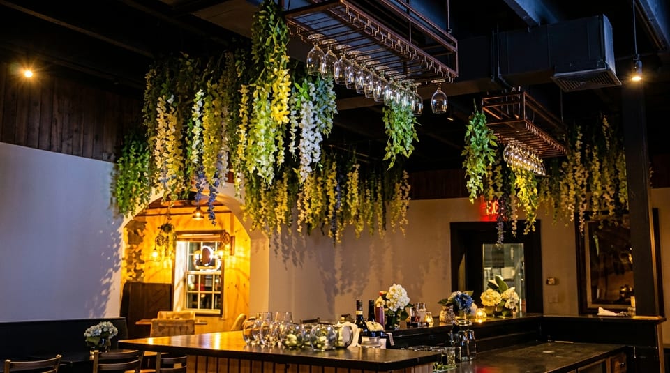 A dimly lit bar area with hanging floral decorations, wine glasses, and bottles on the counter.