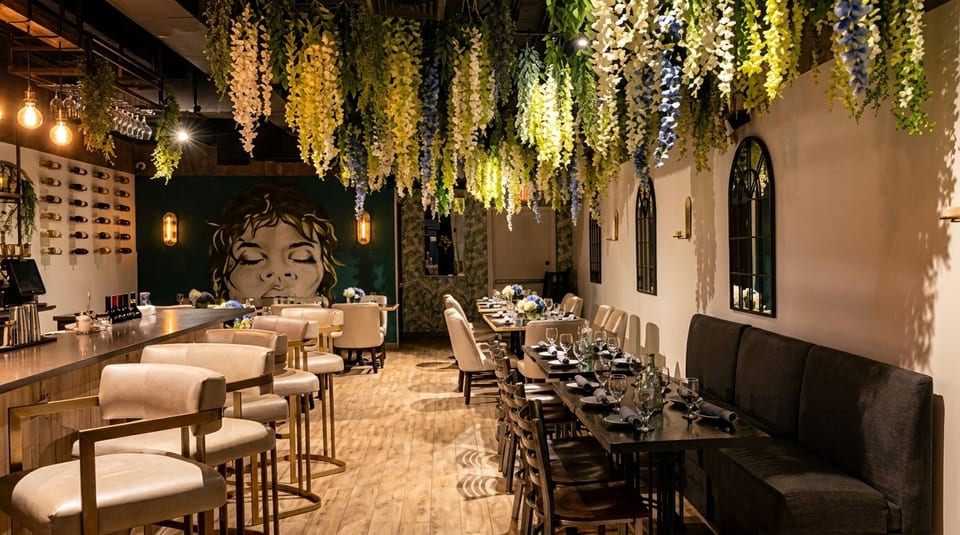A restaurant interior with hanging wisteria, a bar, dining tables, and a large mural.